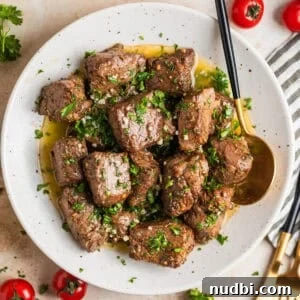 Crispy Air Fryer Steak Bites with Garlic Butter Dip 13 White plate with air fryer steak bites in lemon garlic butter sauce with fresh parsley over top.