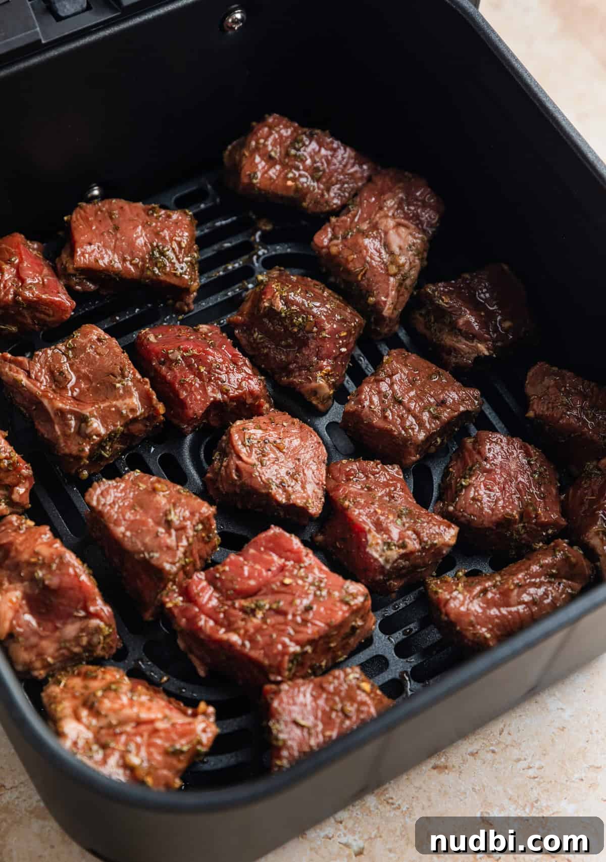 Crispy Air Fryer Steak Bites with Garlic Butter Dip 8 Marinaded sirloin steak bites in air fryer basket before cooking.