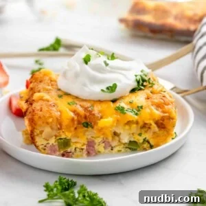 Breakfast casserole with tator tots on white plate with parsley and sour cream.