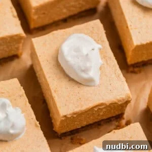 Pumpkin cheesecake bars arranged on brown parchment topped with a dollop of whipped cream.