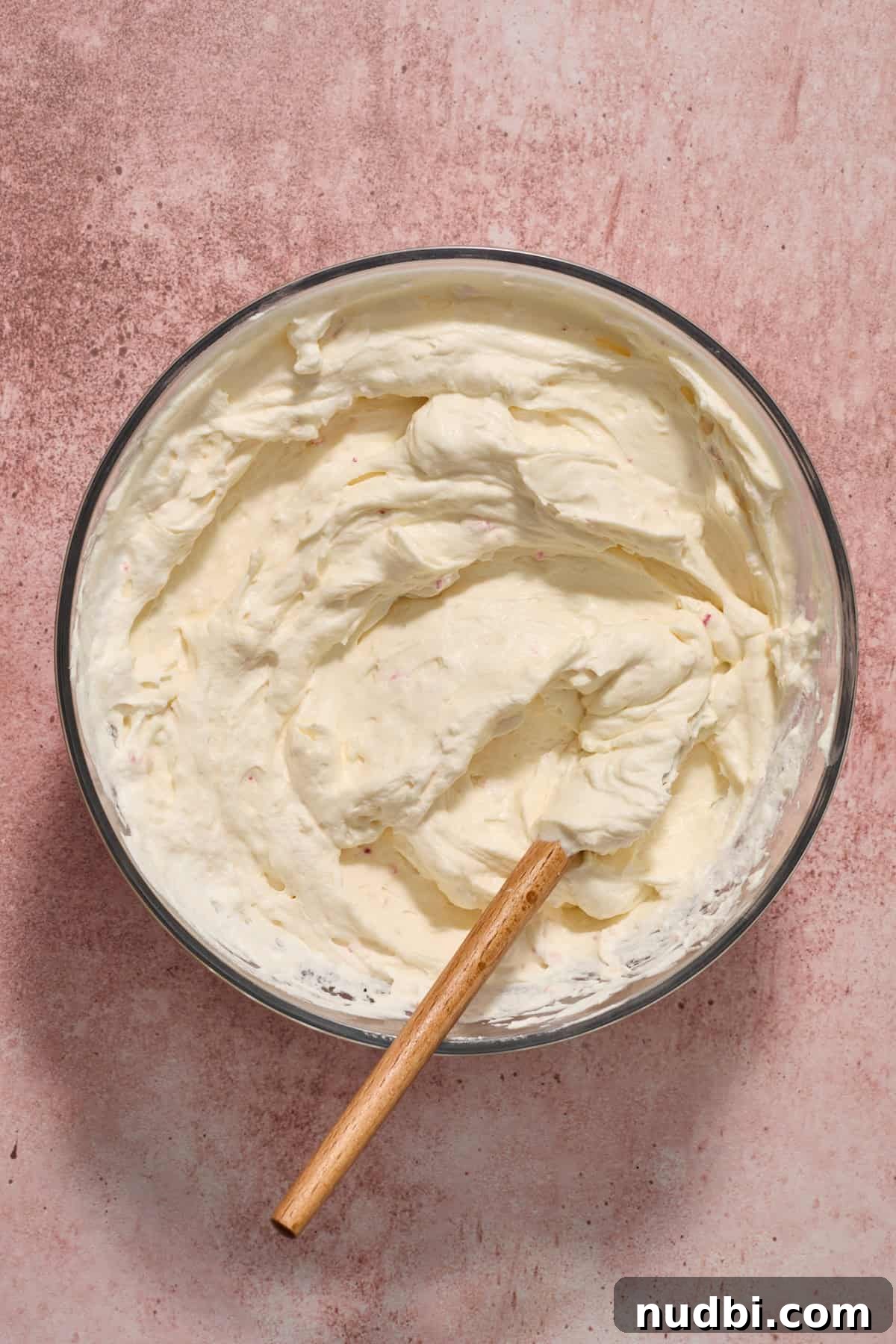 No‑Bake Peppermint Oreo Cheesecake Recipe for the Holidays 13 Crushed peppermints and whipped cream folded into cream cheese mixture in bowl with spatula.
