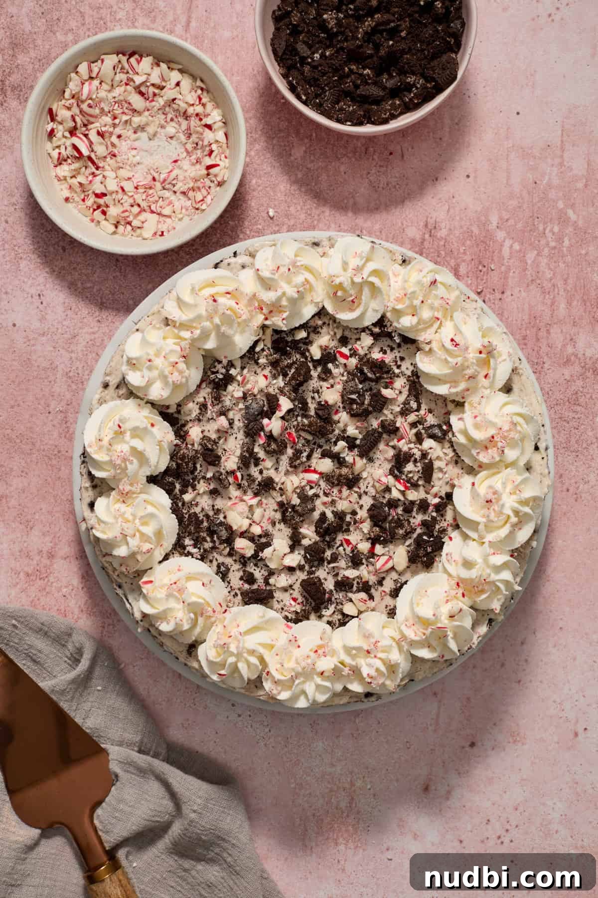 No‑Bake Peppermint Oreo Cheesecake Recipe for the Holidays 17 Ready to serve Oreo peppermint cheesecake topped with whipped cream edges and extra candy canes and cookies sprinkled over top.