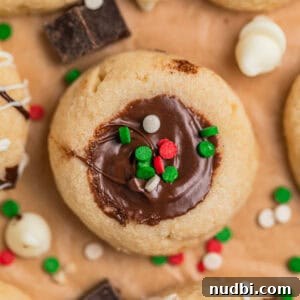 Top Christmas Cookie Recipes to Bake This Holiday Season 10 Nutella thumbprint cookies on parchment topped with red, white and green sprinkles.