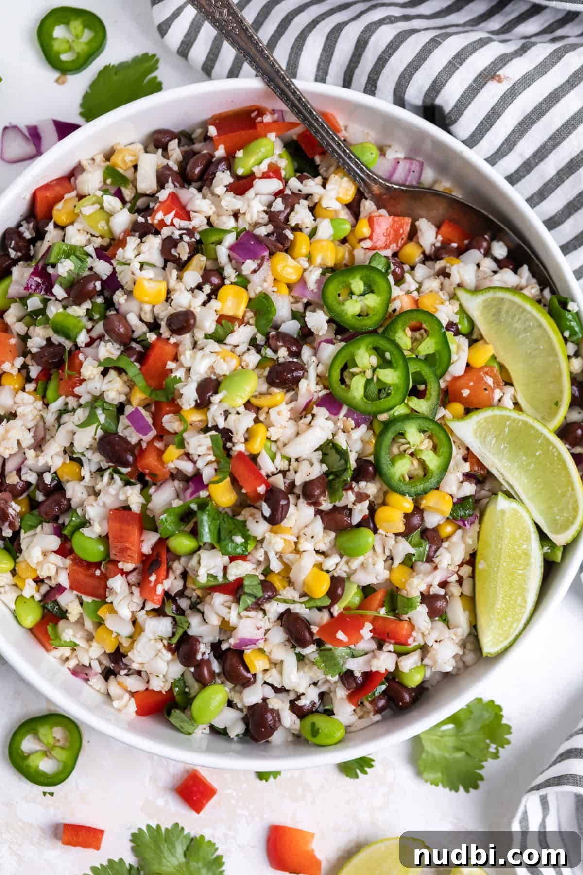 Black Bean & Cauliflower Rice Salad with Zesty Lime Dressing 2 White salad bowl with cauliflower rice salad with black beans, corn, cilantro and serving spoon.