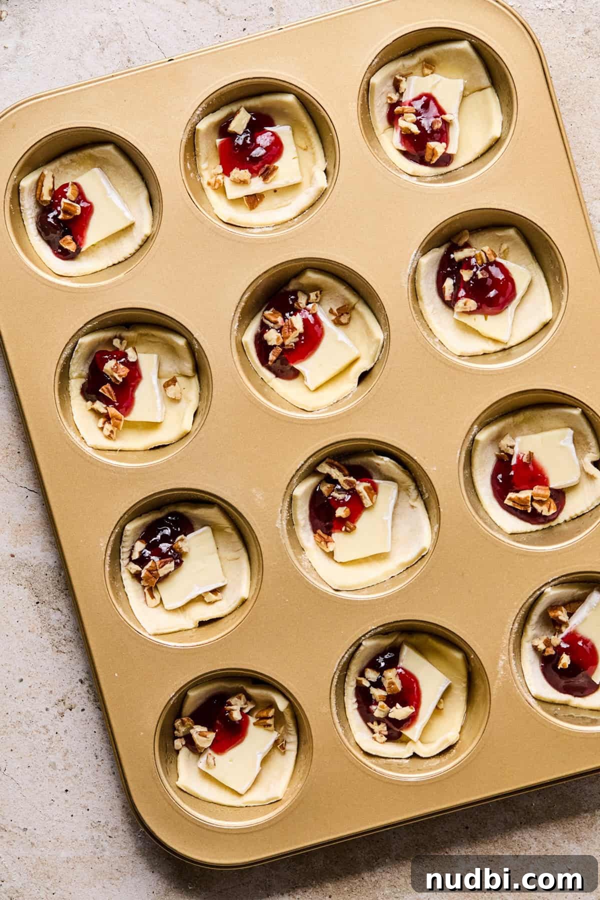 Melted Brie Puff Pastry Bites with Honey & Thyme 6 Puff pastry brie bites topped with jam before baking.