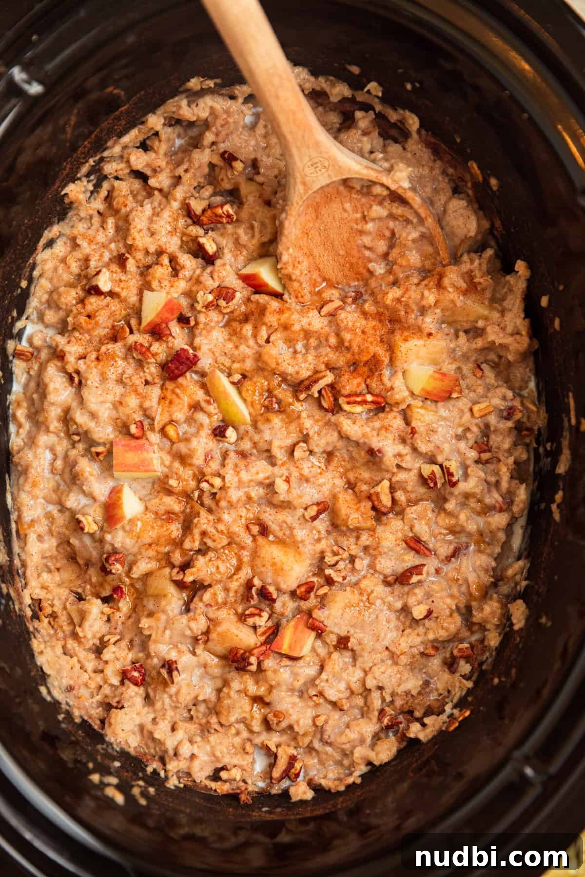Slow Cooker Apple Cinnamon Oatmeal Recipe for Breakfast 7 Cooked oatmeal topped with pecans and cinnamon with wood spoon scooping in.