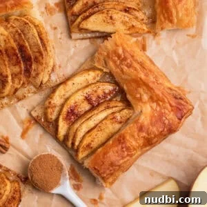 Overhead view of apple tarts on parchment with spoonful of cinnamon beside.