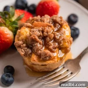 Baked French toast muffin with streusel topping on plate with maple syrup poured over top.
