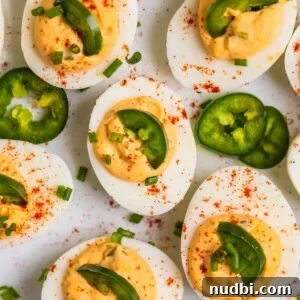 Festive Holiday Appetizers and Party Snacks Guide 11 Deviled eggs on white serving dish topped with chopped chives, jalapeño, and paprika.