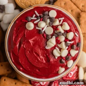 Overhead view of red velvet cake dip in bowl with sprinkles and chocolate chips over top.