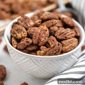 Festive Holiday Appetizers and Party Snacks Guide 22 Bowl of candied pumpkin spiced pecans with striped linen and pan behind it.