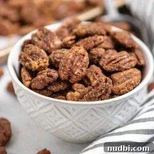 Bowl of candied pumpkin spiced pecans with striped linen and pan behind it.