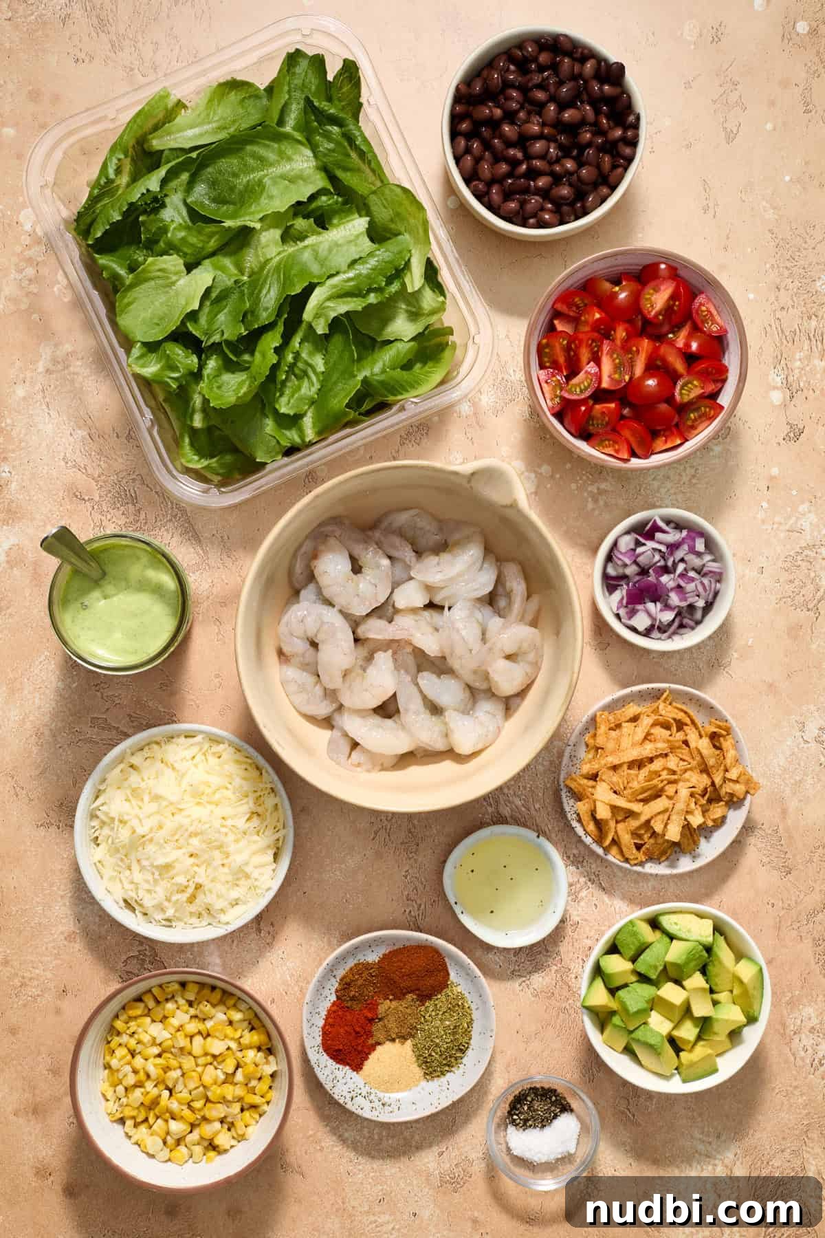 Shrimp Taco Salad with Creamy Cilantro-Lime Dressing 3 Uncooked shrimp, tomatoes, lettuce, beans and other taco salad ingredients arranged on surface.