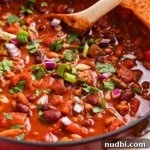 30-Minute Dinner Recipes You'll Love 13 Red dutch oven with ground turkey chili topped with red onion, green onion and cilantro with wooden spoon sitting in pot.