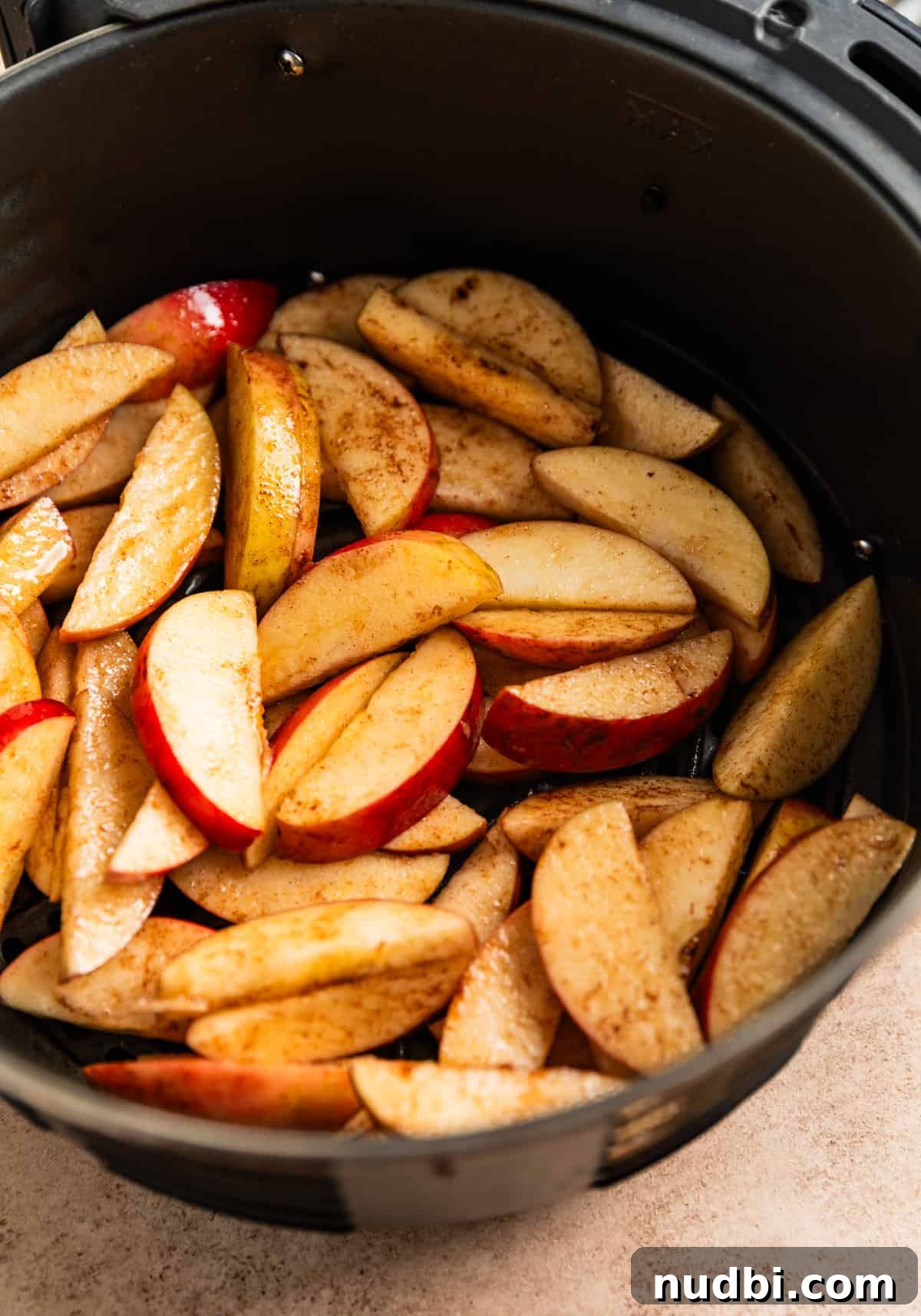 Crispy Caramelized Apples in the Air Fryer 4 Air fryer basket with sliced apples tossed in oil and cinnamon before cooking.