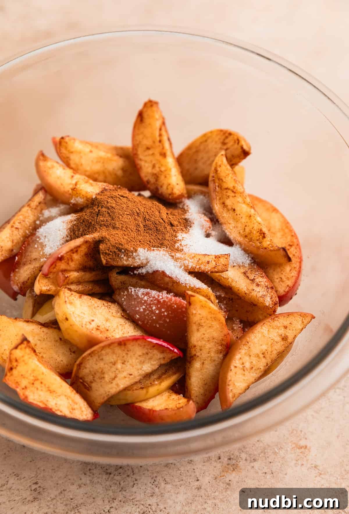 Crispy Caramelized Apples in the Air Fryer 6 Air fryer cinnamon apples in glass mixing bowl with melted butter, sugar and cinnamon poured on top.