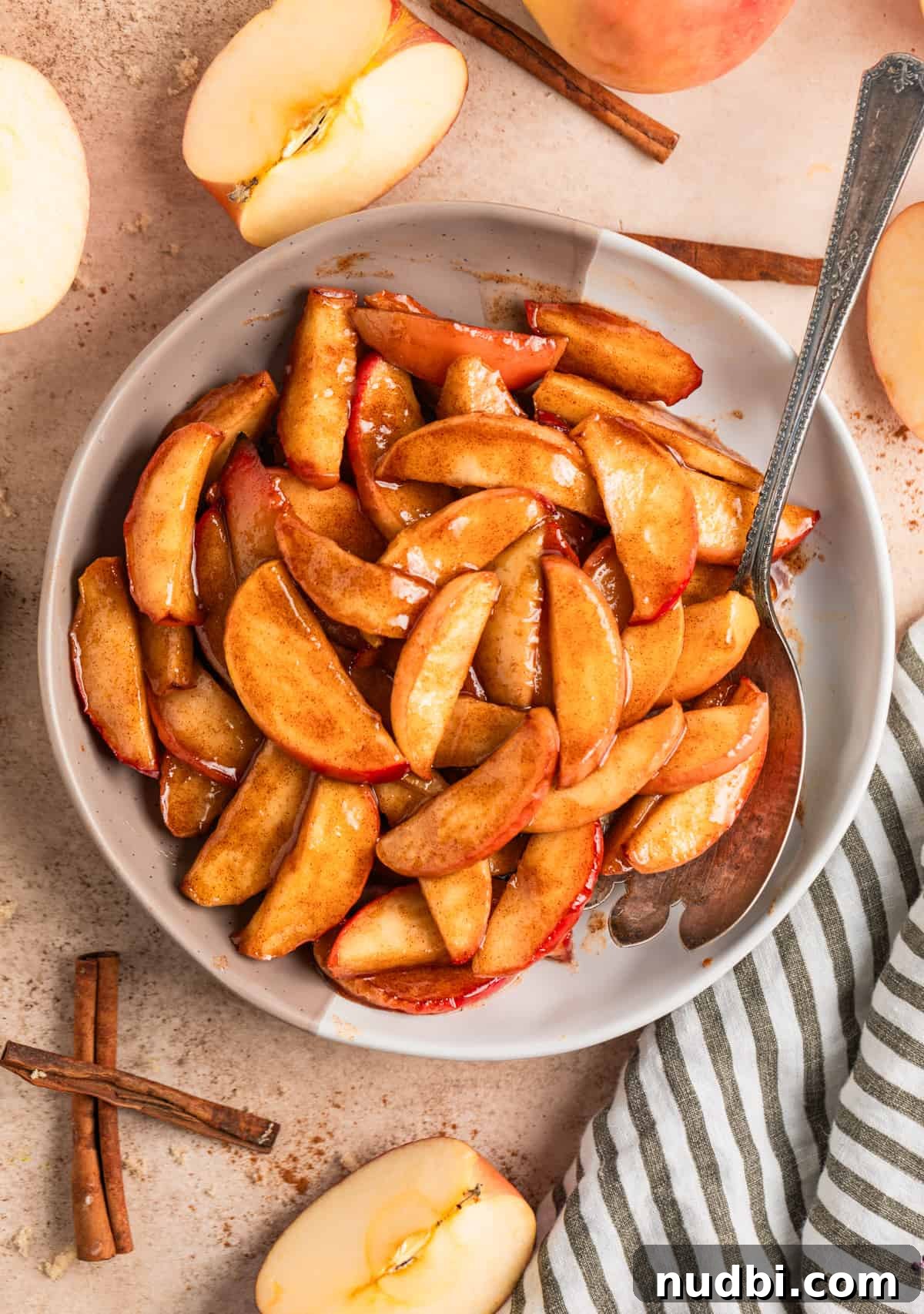 Crispy Caramelized Apples in the Air Fryer 9 Serving plate with buttery cinnamon fried apples with serving spoon and cinnamon sticks beside dish.
