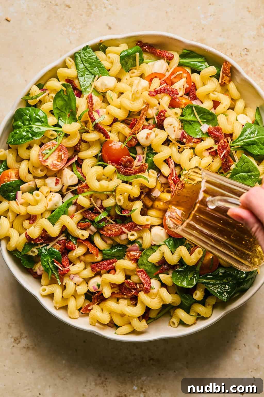 Sun-Dried Tomato Pasta Salad with Fresh Basil & Feta 8 Pasta salad with dressing being poured over top.