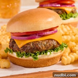 Air fried hamburger on bun with french fries on parchment lined wood surface.