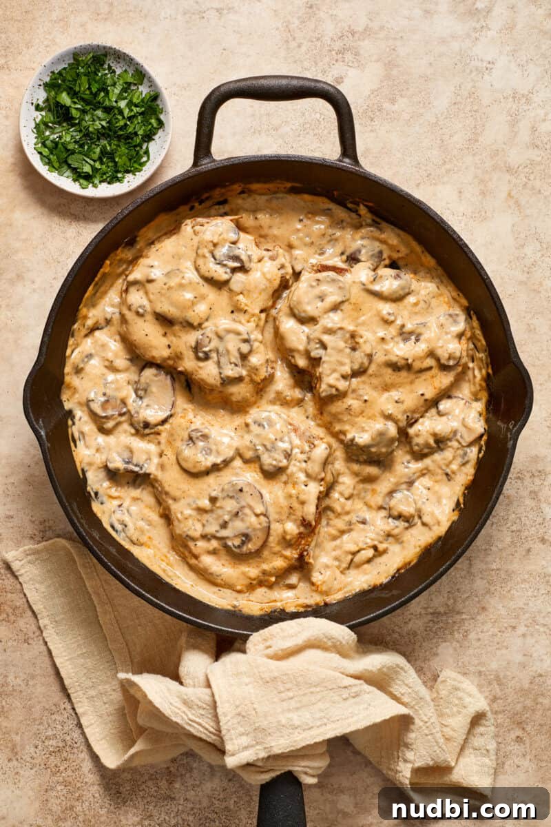 Creamy Mushroom Pork Chops with Garlic and Thyme 12 Cast iron skillet with creamy mushroom bone in pork chops and bowl of parsley beside it.