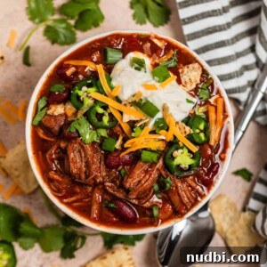 Cozy Dinner Recipes for Comforting Weeknight Meals 24 Overhead view of shredded beef chili topped with sour cream, cilantro, cheese and more.