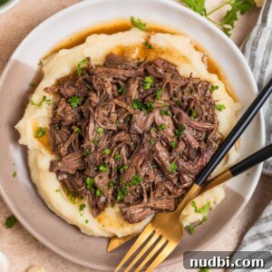 Cozy Dinner Recipes for Comforting Weeknight Meals 6 Tan and white plate with crock pot shredded beef over mashed potatoes.