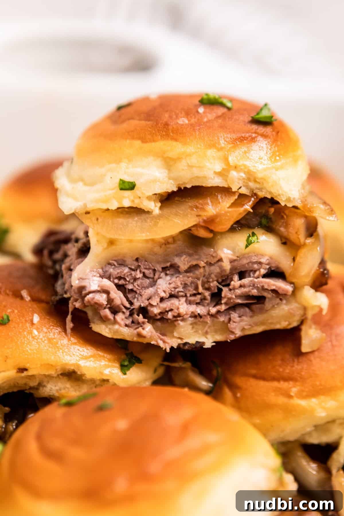 French Dip Sliders Recipe with Savory Au Jus for Dipping 2 French dip slider with roast beef, provolone, onion and mushroom stacked on other sandwiches.