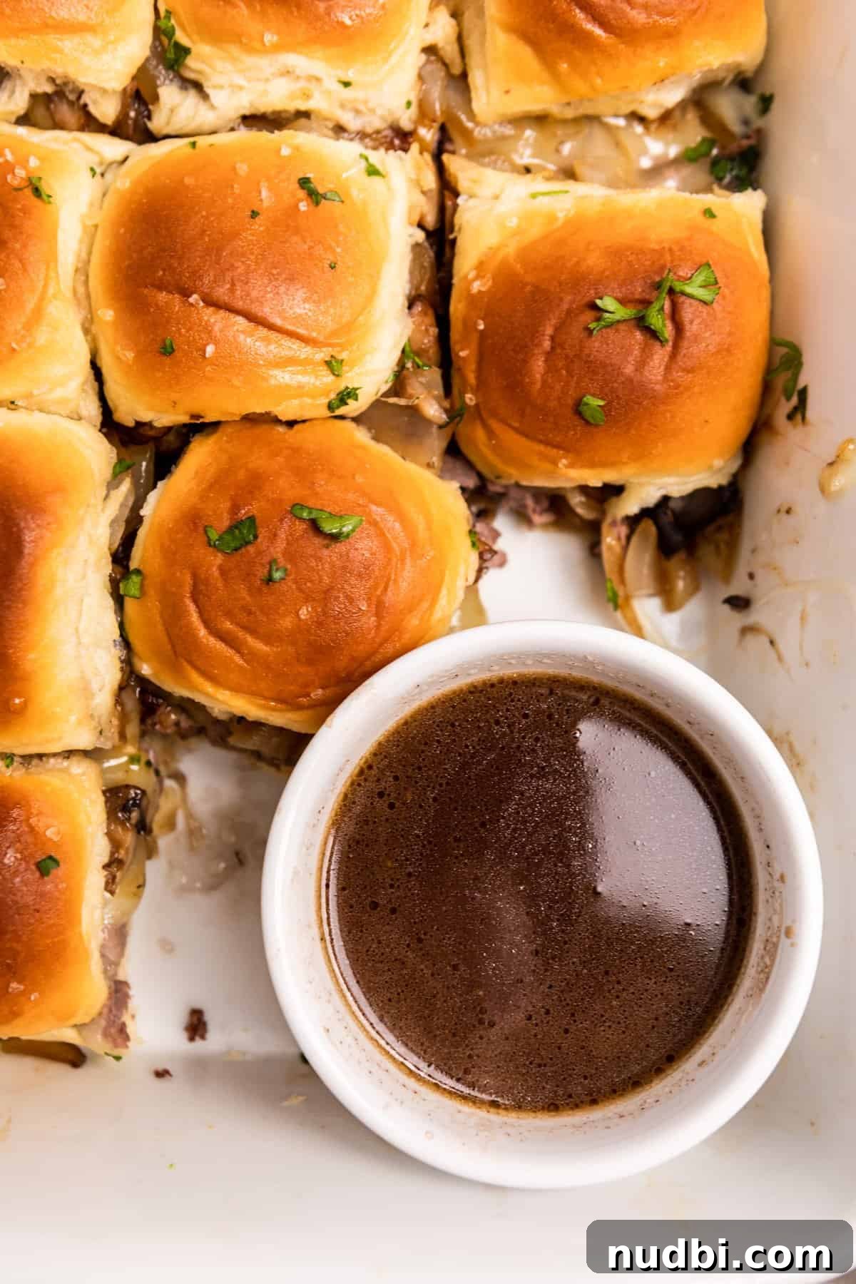 French Dip Sliders Recipe with Savory Au Jus for Dipping 11 Overhead view of au jus in bowl with roast beef sliders surrounding it.