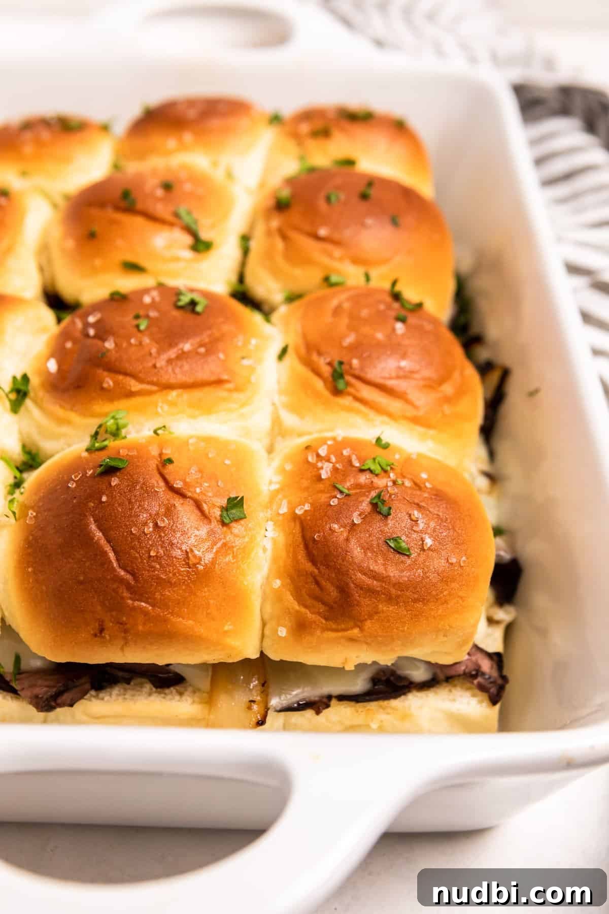 French Dip Sliders Recipe with Savory Au Jus for Dipping 13 White baking dish with fresh French dip sliders topped with parsley.