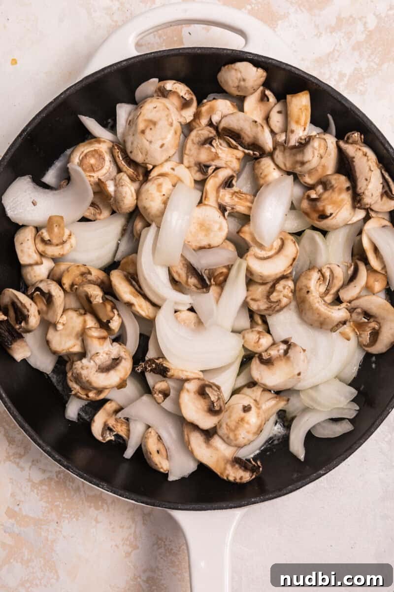 French Dip Sliders Recipe with Savory Au Jus for Dipping 3 Overhead view of cast iron skillet with raw onion and mushrooms in butter.