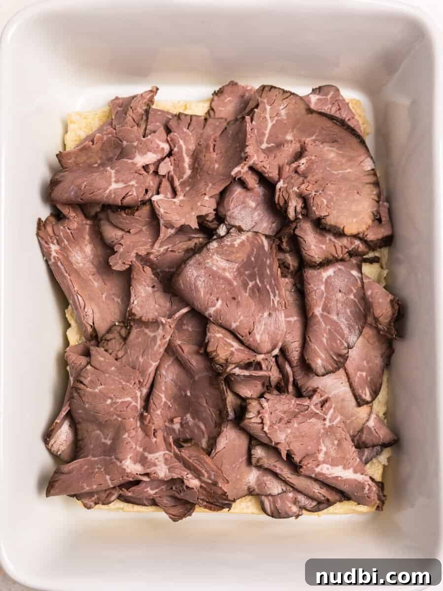 French Dip Sliders Recipe with Savory Au Jus for Dipping 6 Roast beef slices layered on top of Hawaiian rolls in baking dish.