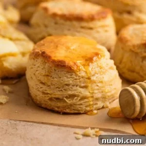 Simple honey biscuits on tan parchment with honey drizzling over top with honey dipper stick beside it.