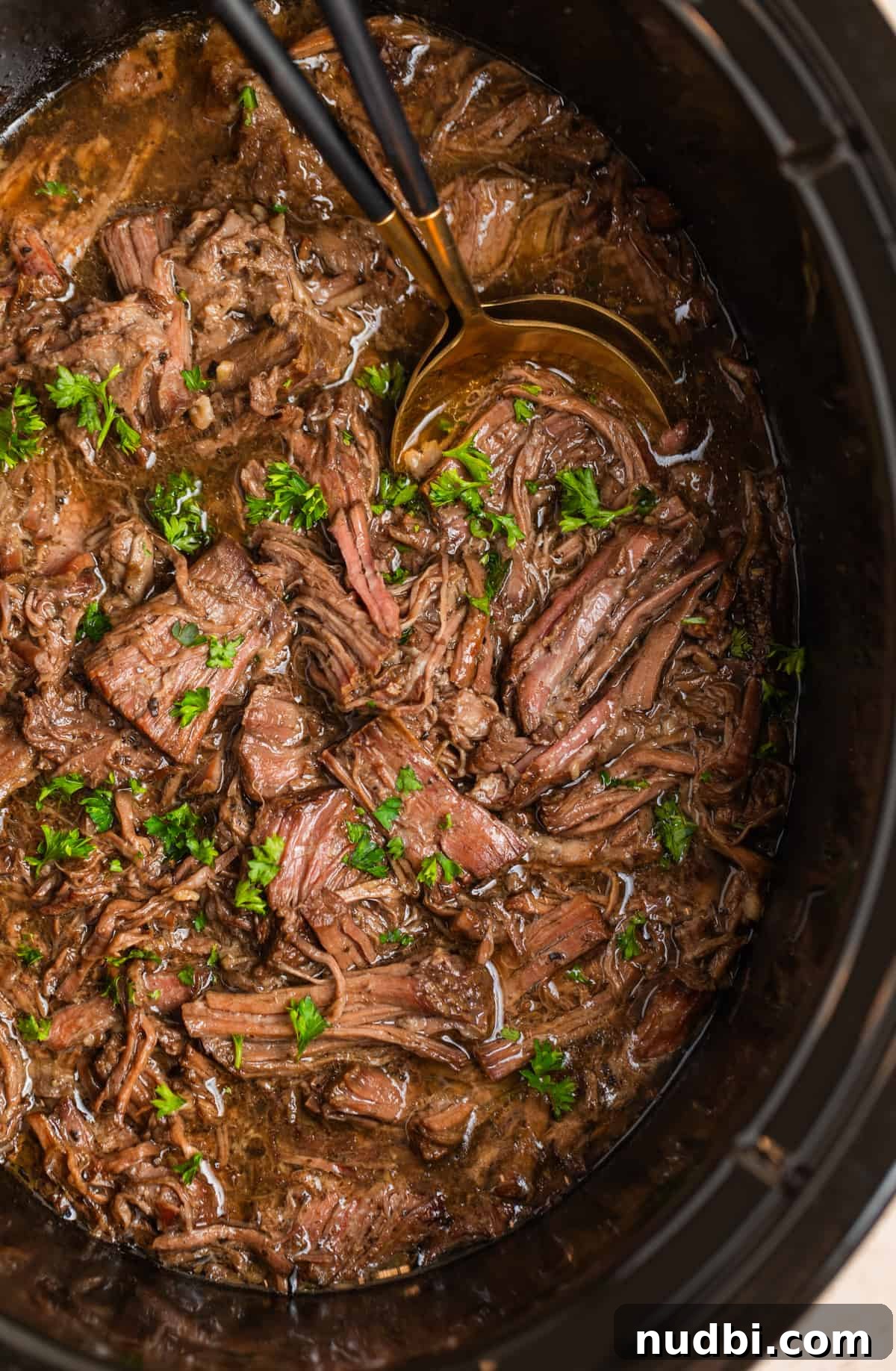Slow-Cooker Shredded Beef Recipe for Tender, Flavorful Meals 4 Slow cooker shredded beef in crockpot with serving utensils and chopped parsely.