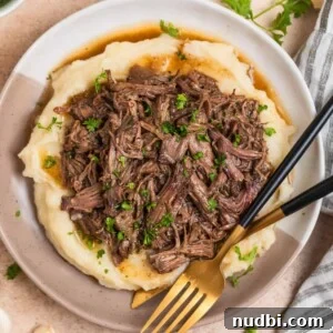 Slow-Cooker Shredded Beef Recipe for Tender, Flavorful Meals 10 Tan and white plate with crock pot shredded beef over mashed potatoes.