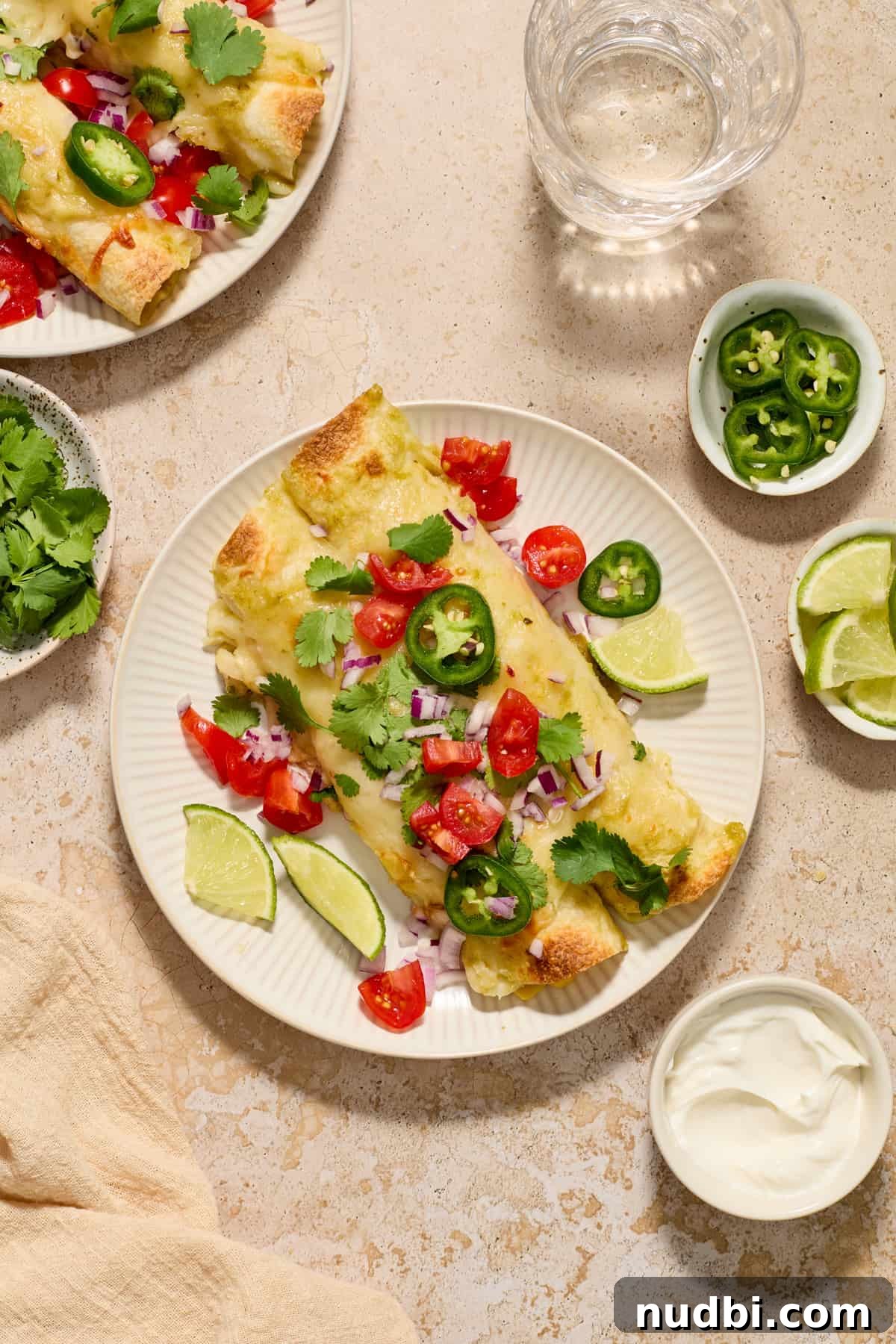 Authentic Green Salsa Chicken Enchiladas Recipe 12 Chicken enchiladas on white plate topped cilantro, tomatoes and jalapeños.