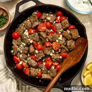 Cast iron skillet with steak bites and cherry tomatoes topped with feta cheese.