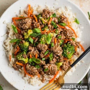 White plate with beef teriyaki served over white rice and topped with chopped green onions and toasted sesame seeds.