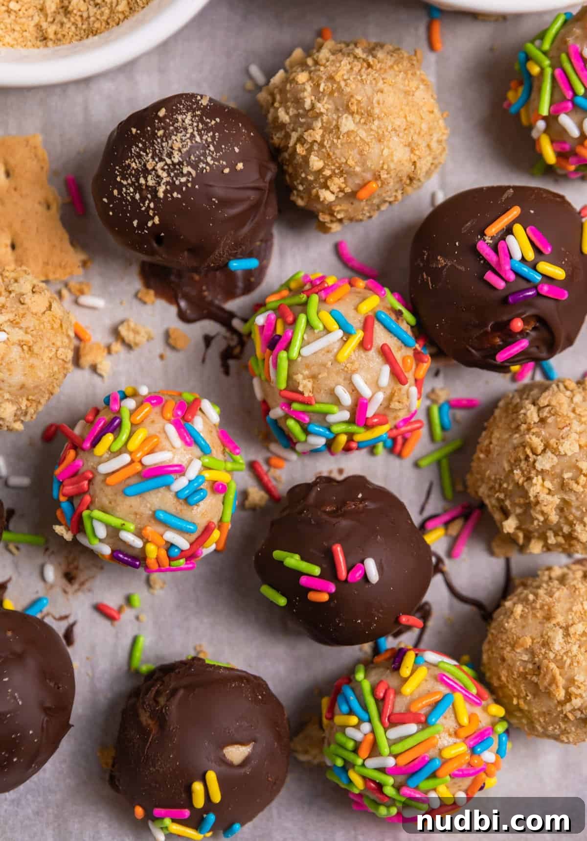 No-Bake Mini Cheesecake Bites: Easy Dessert Balls Recipe 3 Variety of coated no bake cheesecake balls on parchment with sprinkles, graham cracker crumbs and chocolate.