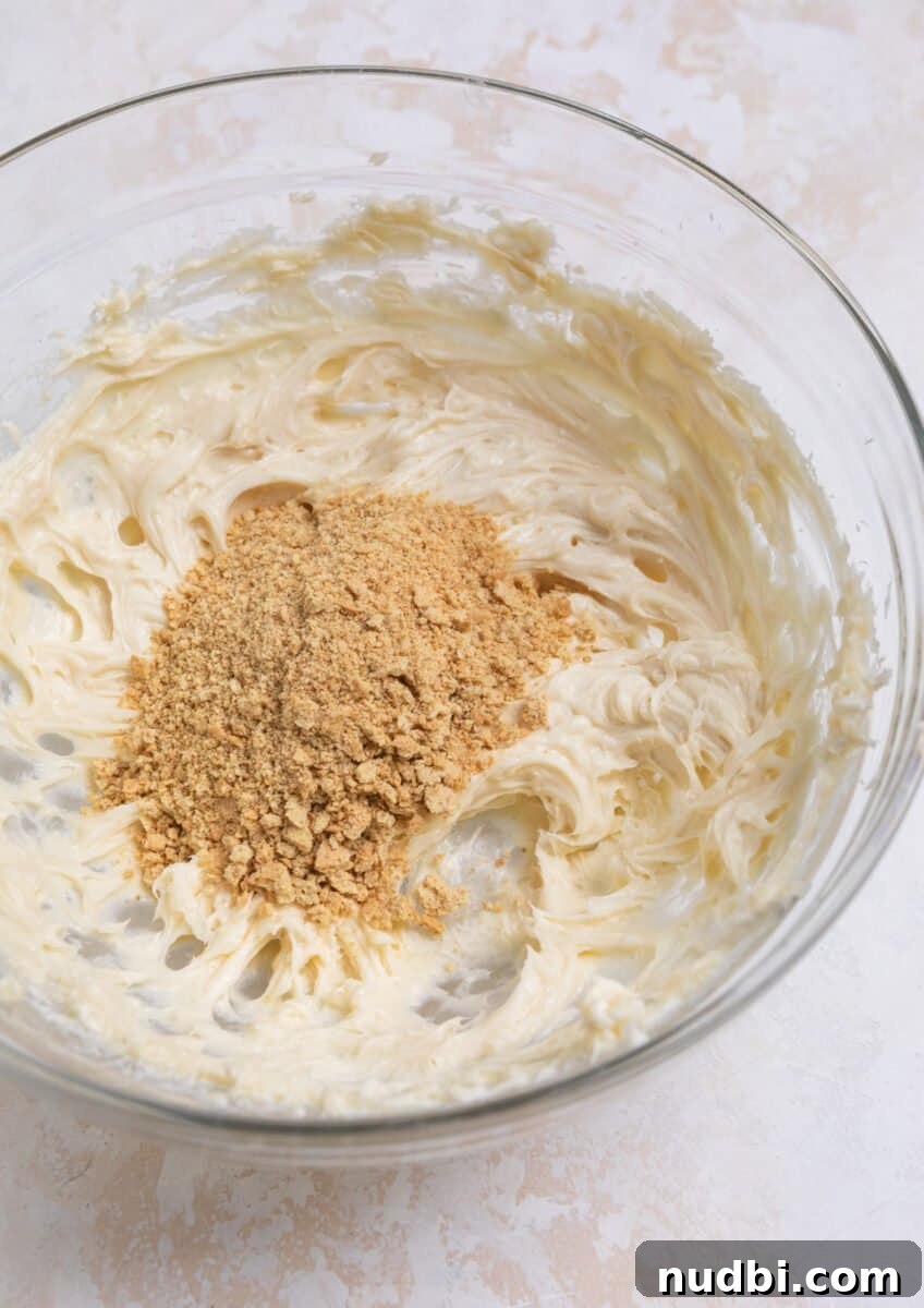 No-Bake Mini Cheesecake Bites: Easy Dessert Balls Recipe 5 Crushed graham crackers poured into mixing bowl with cheesecake mixture.