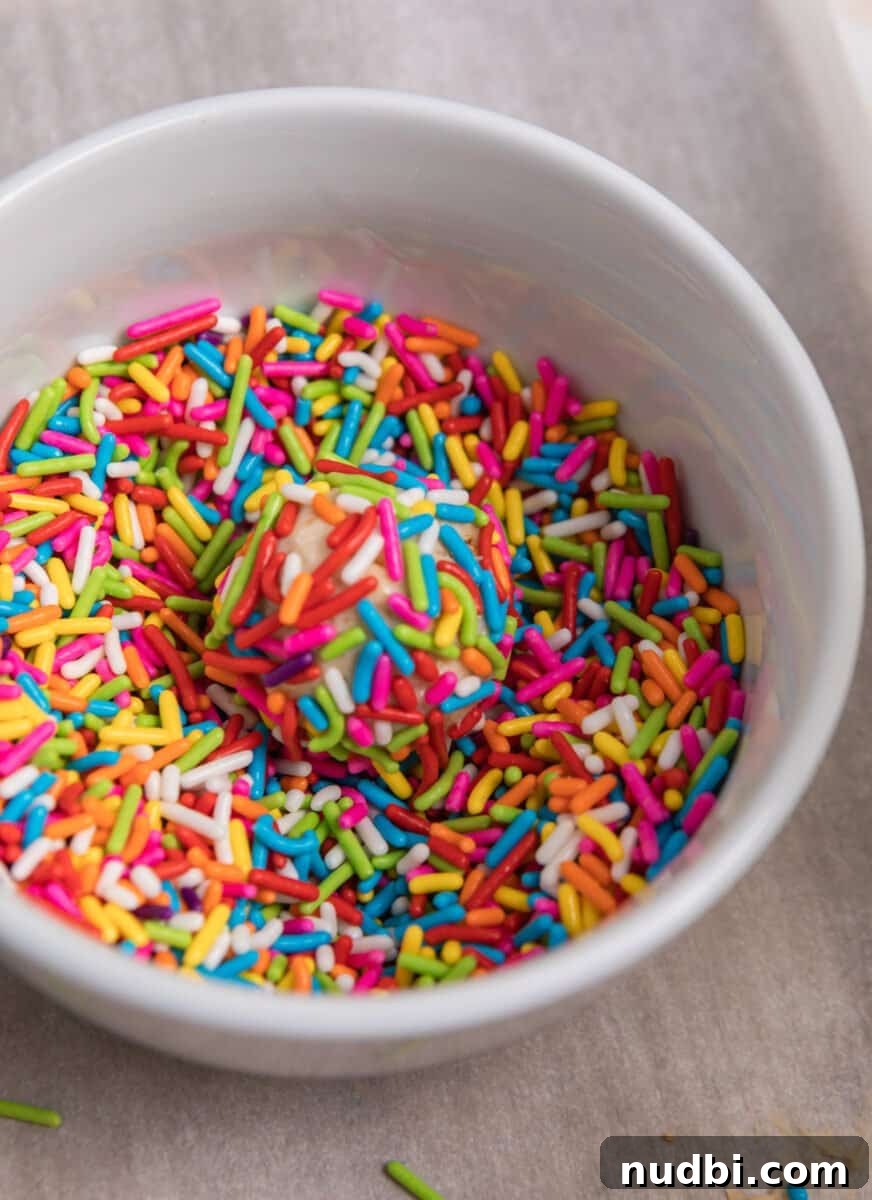 No-Bake Mini Cheesecake Bites: Easy Dessert Balls Recipe 8 Cheesecake ball dipped in bowl of sprinkles.