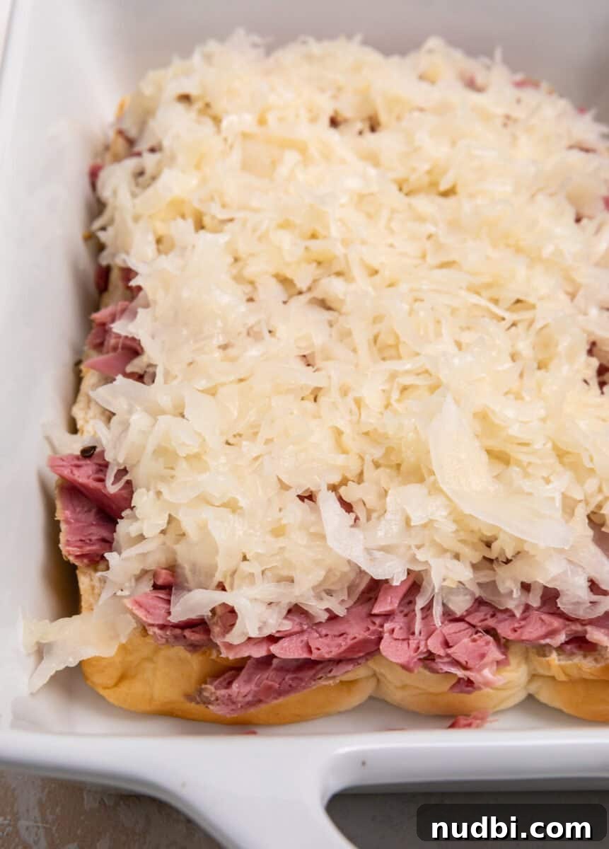 Classic Reuben Sliders with Melted Swiss and Tangy Sauerkraut 7 Sauerkraut on top of corned beef and rolls in white baking dish.