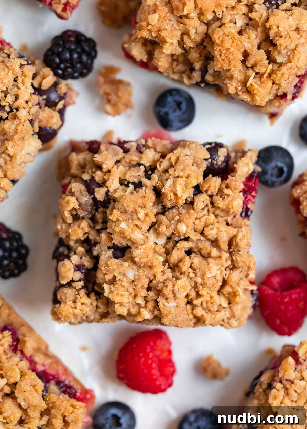 Mixed Berry Crumble Bars Recipe with Oat Streusel Topping 7 Mixed berry oat bars with crumble topping on white background with fresh berries and crumbles surrounding.