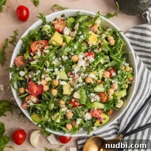 Chickpea avocado salad in bowl with arugula, feta, cucumbers, tomato and other ingredients.