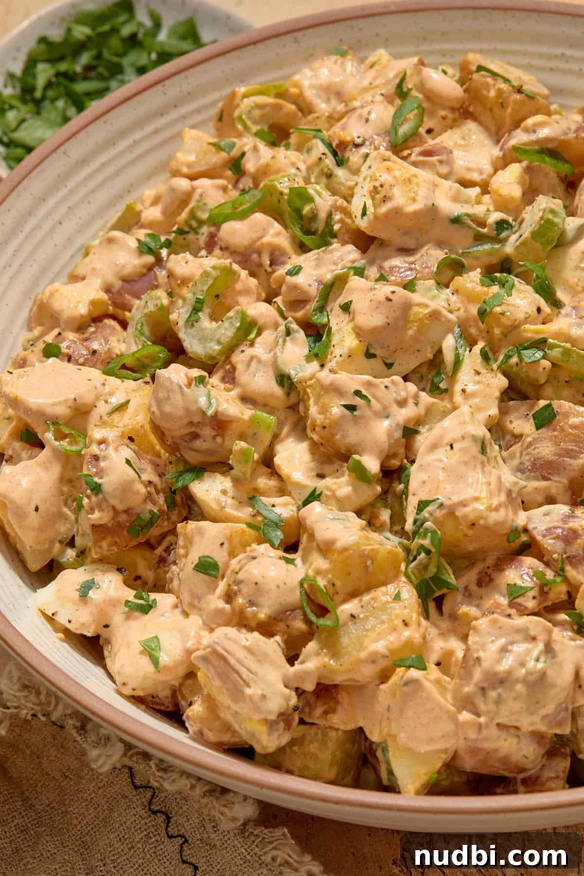 Cajun Potato Salad Recipe with Zesty Dressing and Bacon 10 Cajun potato salad in bowl topped with chopped parsley.