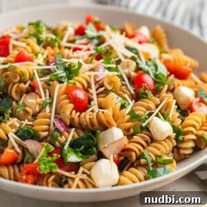 Pasta salad made with grape tomatoes, spinach, basil, mozzarella and other ingredients in serving bowl.
