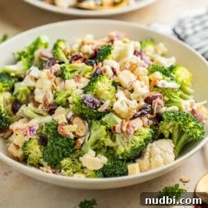 Broccoli cauliflower salad in bowl tossed with cheese, cranberries, bacon and more.