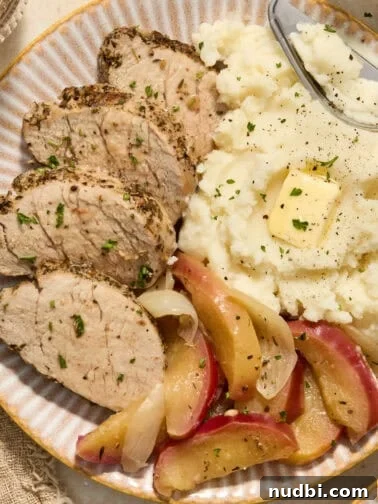 Pork tenderloin sliced on plate with apples and mashed potatoes.