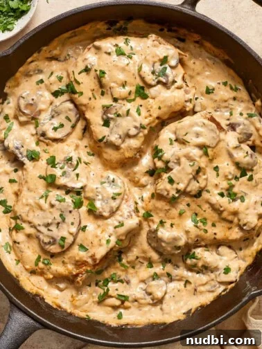 Skillet with cream of mushroom pork chops topped with chopped parsley.