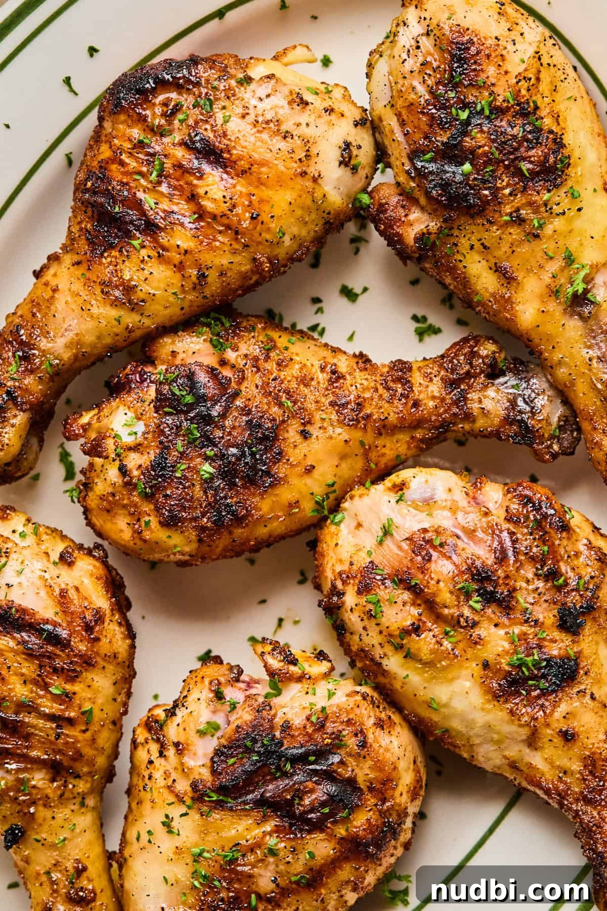 Crispy Grilled Chicken Drumsticks with Smoky BBQ Flavor 2 Grilled chicken legs on plate with chopped parsley.