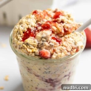 Jar of strawberry cheesecake overnight oatmeal with white spoon and oats on counter surrounding.